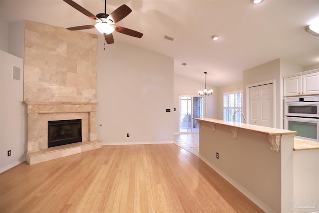 unfurnished living room with ceiling fan with notable chandelier, sink, light hardwood / wood-style flooring, vaulted ceiling, and a fireplace