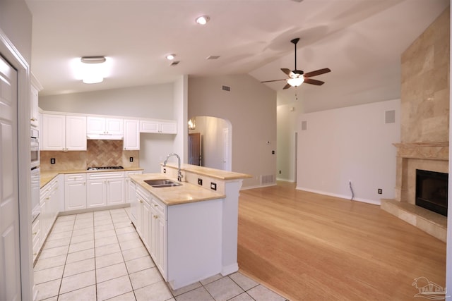 kitchen featuring sink, a tile fireplace, a center island with sink, light hardwood / wood-style flooring, and white cabinets