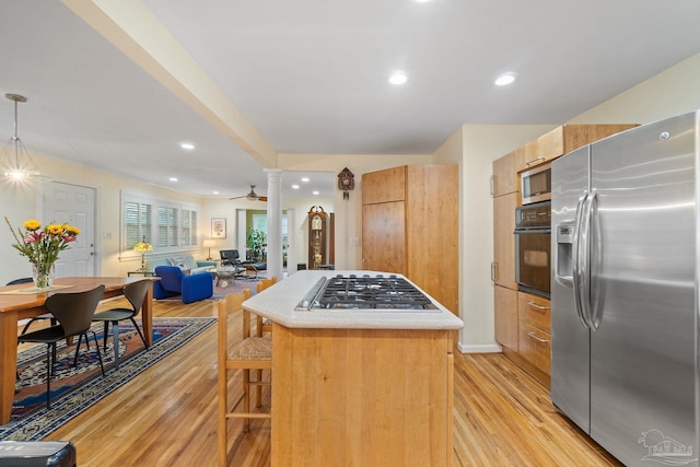 kitchen featuring ceiling fan, hanging light fixtures, stainless steel appliances, decorative columns, and light hardwood / wood-style floors