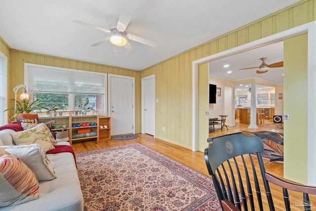 living room with ceiling fan, wood-type flooring, and wooden walls