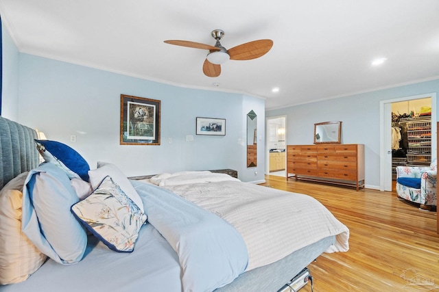 bedroom with a walk in closet, crown molding, ceiling fan, light wood-type flooring, and a closet