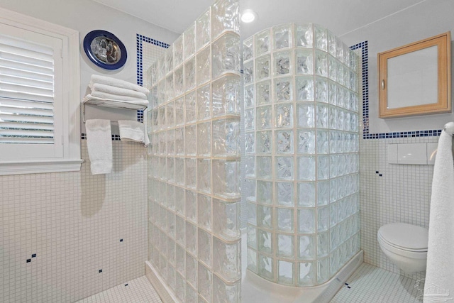 bathroom with tile patterned flooring, tiled shower, toilet, and tile walls