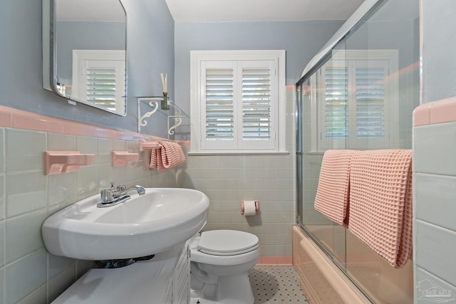 full bathroom featuring shower / bath combination with glass door, toilet, tile walls, and sink