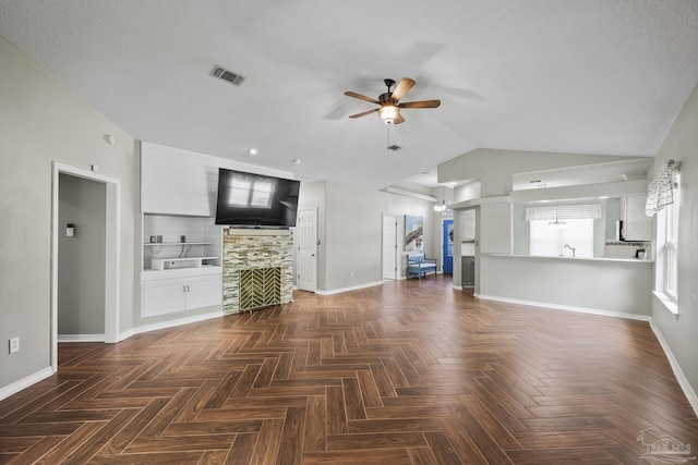unfurnished living room featuring lofted ceiling, visible vents, baseboards, a ceiling fan, and a stone fireplace