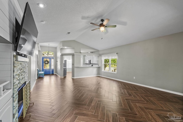 unfurnished living room featuring lofted ceiling, visible vents, baseboards, a stone fireplace, and ceiling fan with notable chandelier