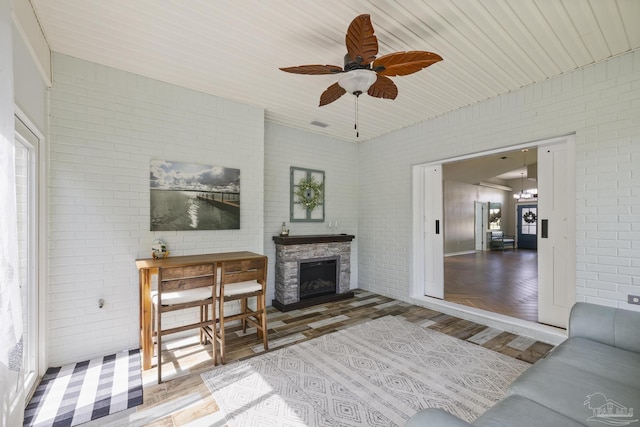 living area featuring ceiling fan, brick wall, and a fireplace