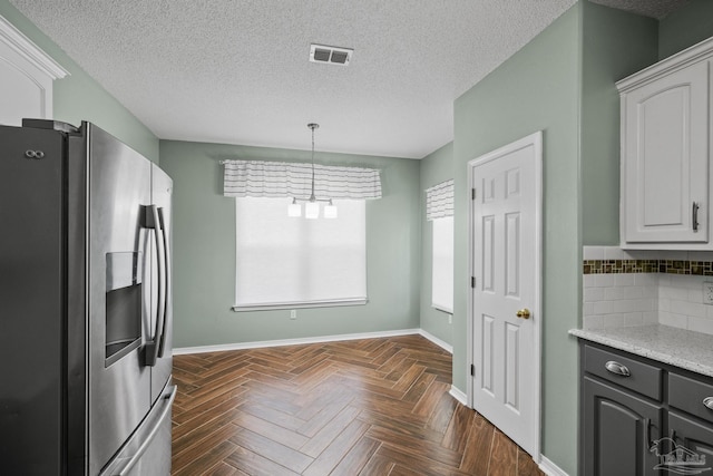 kitchen with visible vents, light countertops, baseboards, stainless steel refrigerator with ice dispenser, and backsplash