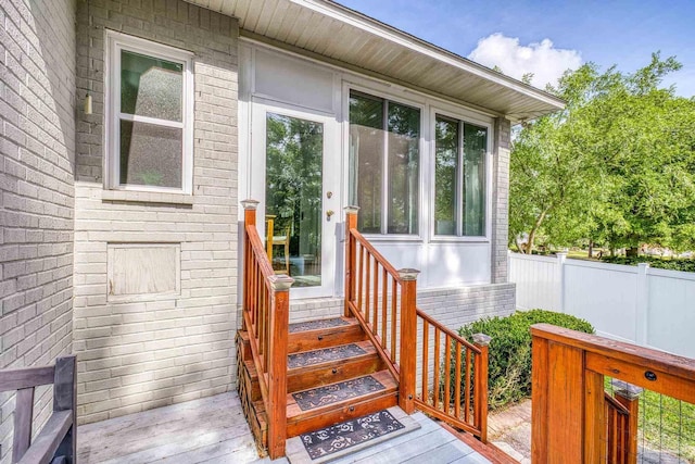 doorway to property featuring brick siding, a deck, and fence