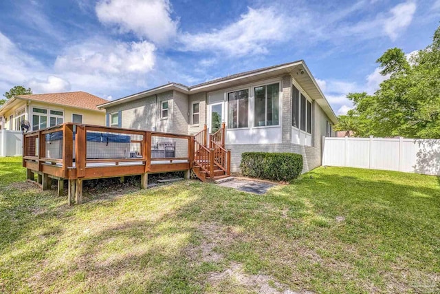back of property with a sunroom, a wooden deck, a lawn, brick siding, and fence