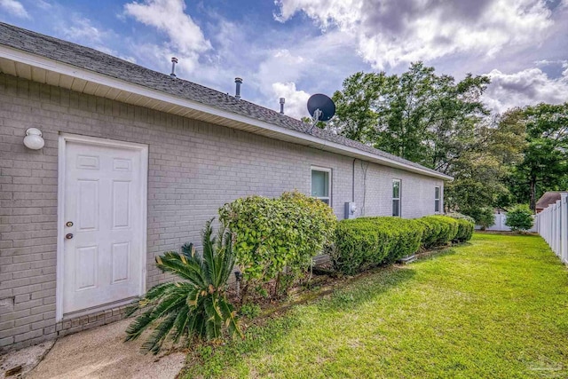 view of side of home with brick siding, fence, and a yard