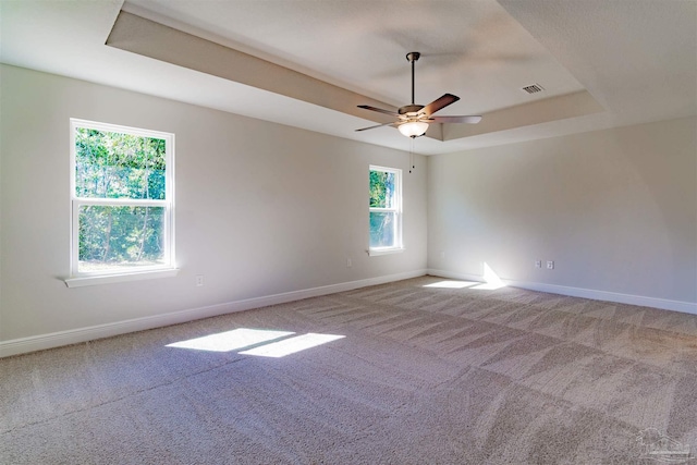 carpeted empty room featuring ceiling fan and a raised ceiling