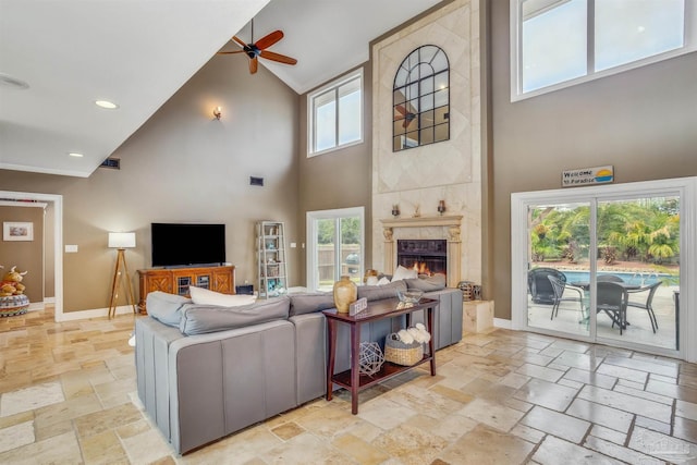 living room with a tiled fireplace, ceiling fan, high vaulted ceiling, and a healthy amount of sunlight