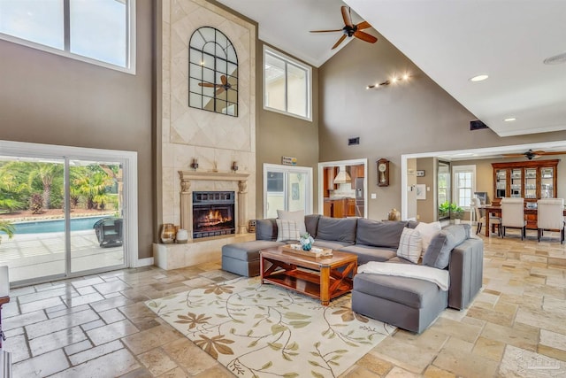 living room with a high end fireplace, ceiling fan, and a high ceiling