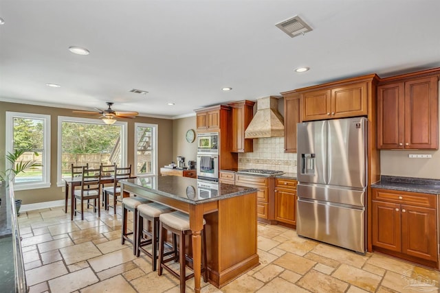 kitchen with a kitchen island, appliances with stainless steel finishes, a kitchen breakfast bar, crown molding, and custom range hood