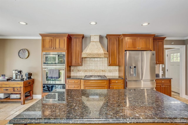 kitchen with appliances with stainless steel finishes, dark stone countertops, decorative backsplash, crown molding, and custom range hood