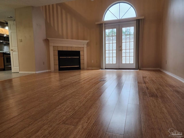 unfurnished living room with light wood-type flooring, a tiled fireplace, french doors, and a towering ceiling