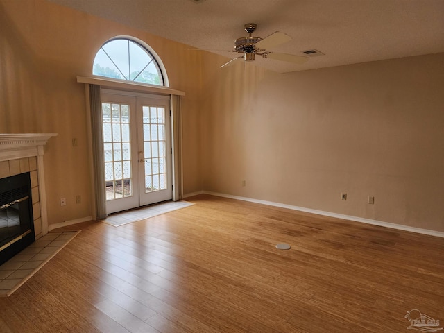 unfurnished living room featuring french doors, a tiled fireplace, a textured ceiling, ceiling fan, and light wood-type flooring