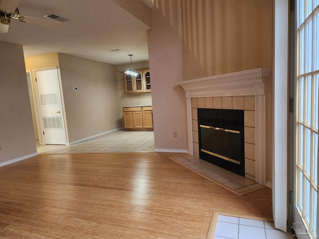 unfurnished living room with a tile fireplace, ceiling fan, and light hardwood / wood-style flooring