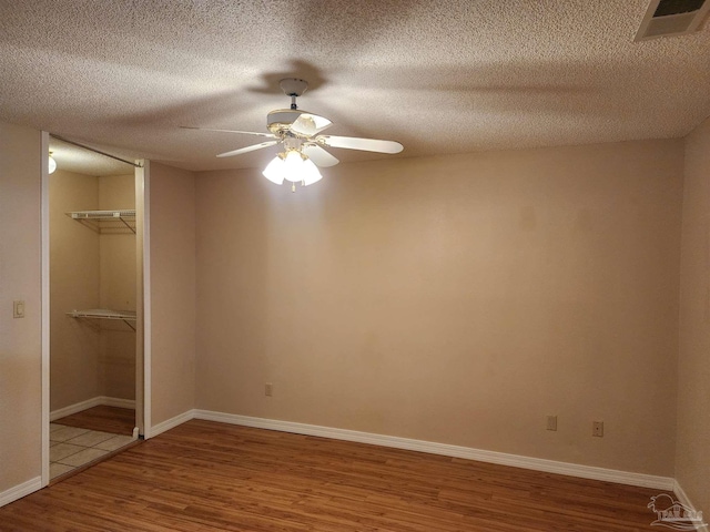 unfurnished bedroom with a textured ceiling, a spacious closet, hardwood / wood-style flooring, and ceiling fan