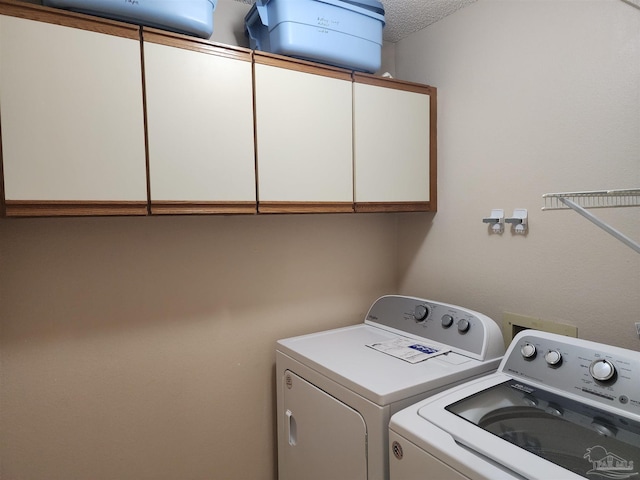 washroom featuring a textured ceiling, washing machine and dryer, and cabinets