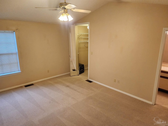 unfurnished bedroom featuring a closet, a walk in closet, light carpet, vaulted ceiling, and ceiling fan