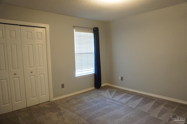 unfurnished bedroom with a textured ceiling, dark colored carpet, and a closet