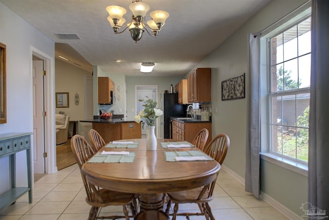 dining room with a textured ceiling, a notable chandelier, light tile patterned flooring, and sink