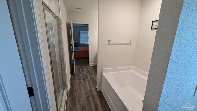 bathroom with a garden tub, a textured wall, wood finished floors, and a shower with shower door