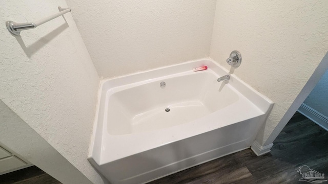 bathroom with a garden tub, a textured wall, and wood finished floors