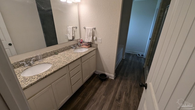 full bathroom featuring double vanity, wood finished floors, a sink, and baseboards