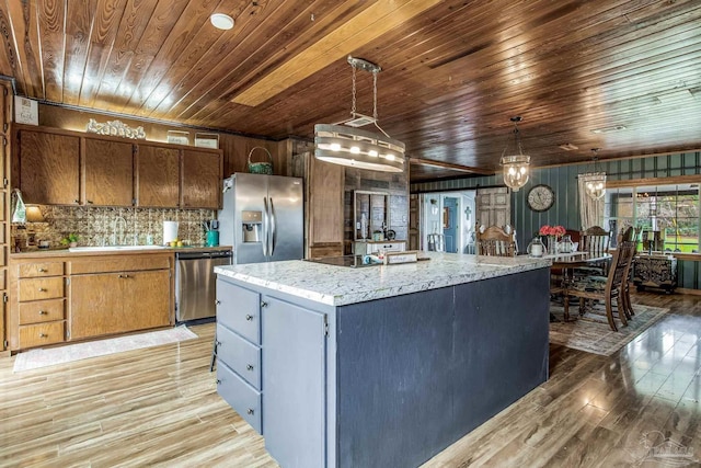 kitchen with light stone countertops, hanging light fixtures, stainless steel appliances, light hardwood / wood-style flooring, and a kitchen island