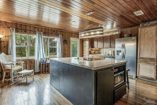 kitchen with dark wood-type flooring, wooden ceiling, wood walls, a kitchen island, and appliances with stainless steel finishes