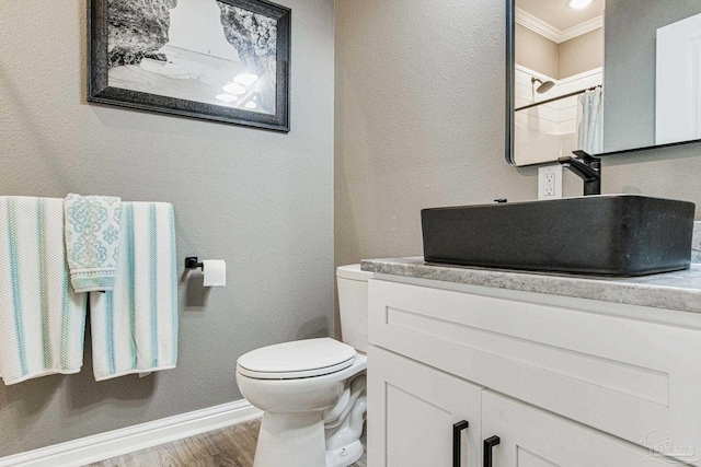 bathroom with baseboards, toilet, wood finished floors, crown molding, and vanity