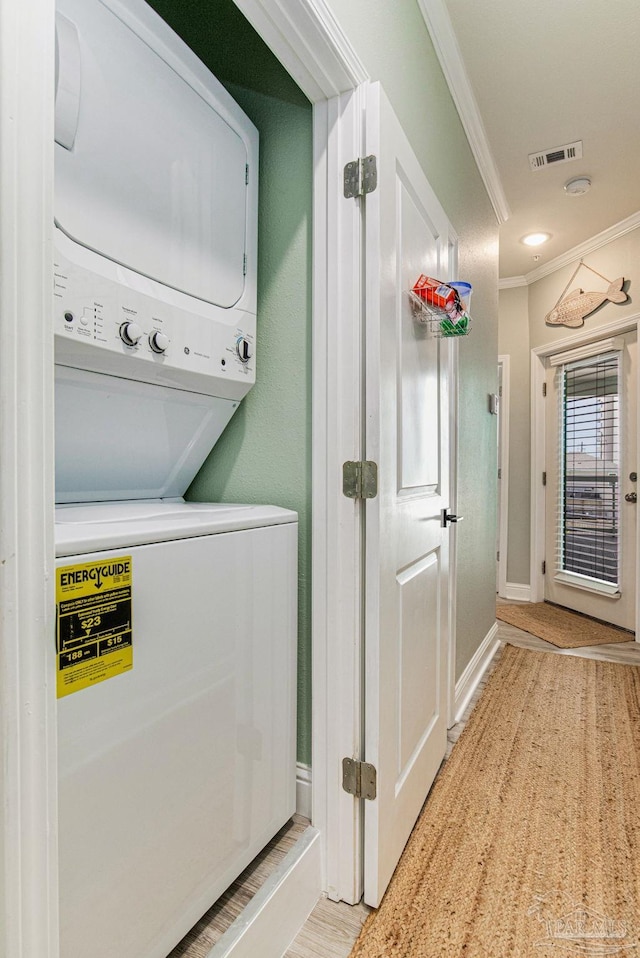 laundry area with laundry area, baseboards, visible vents, crown molding, and stacked washing maching and dryer