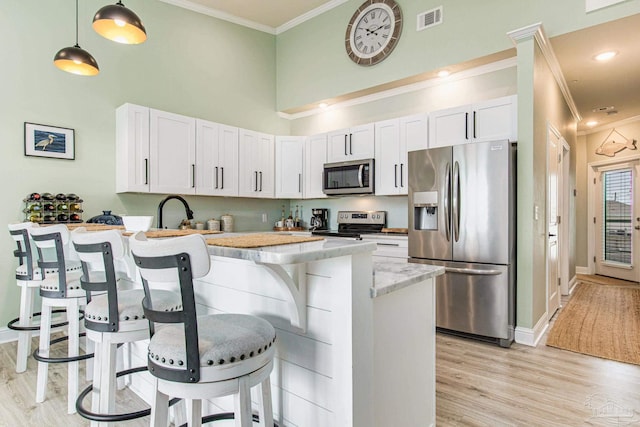 kitchen with visible vents, a peninsula, stainless steel appliances, crown molding, and a kitchen bar