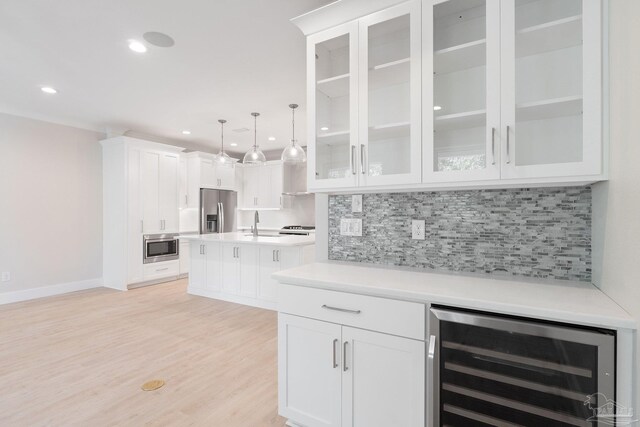 kitchen featuring appliances with stainless steel finishes, light hardwood / wood-style flooring, white cabinets, backsplash, and beverage cooler