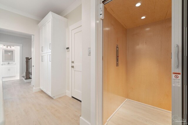 hallway with elevator, sink, light hardwood / wood-style flooring, and crown molding