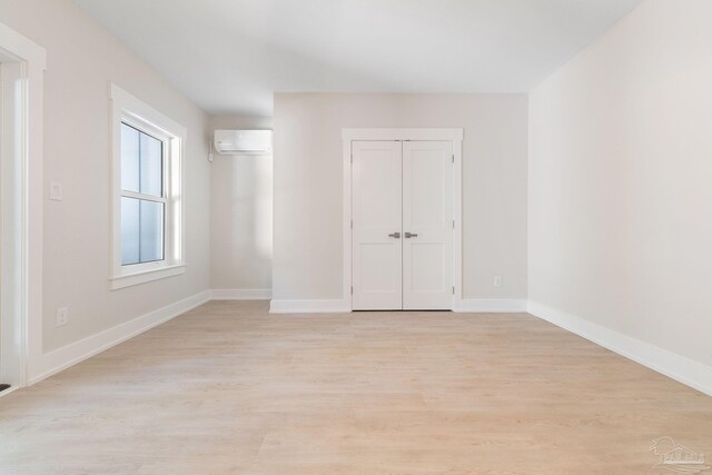 unfurnished bedroom with a wall unit AC and light wood-type flooring