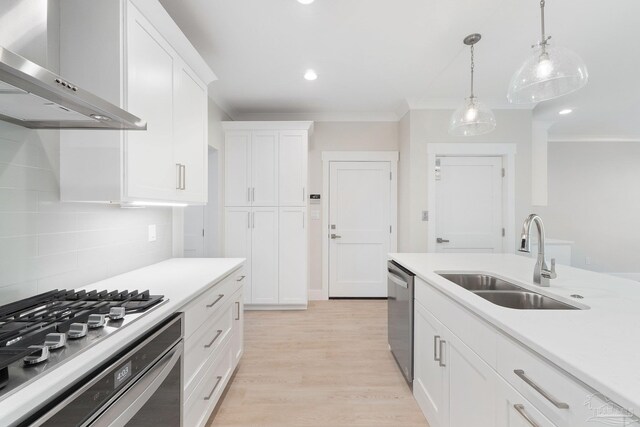 kitchen with tasteful backsplash, wall chimney range hood, white cabinets, sink, and light hardwood / wood-style floors