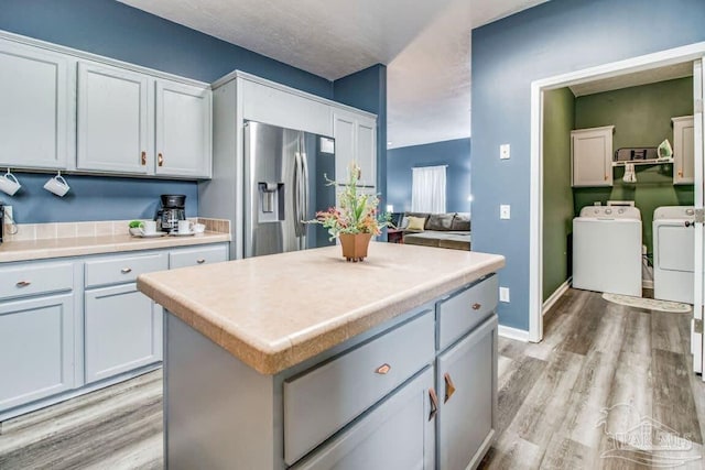 kitchen featuring stainless steel fridge with ice dispenser, light hardwood / wood-style floors, washer and dryer, and white cabinets