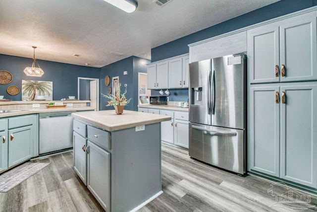 kitchen with sink, decorative light fixtures, a kitchen island, stainless steel appliances, and light hardwood / wood-style floors