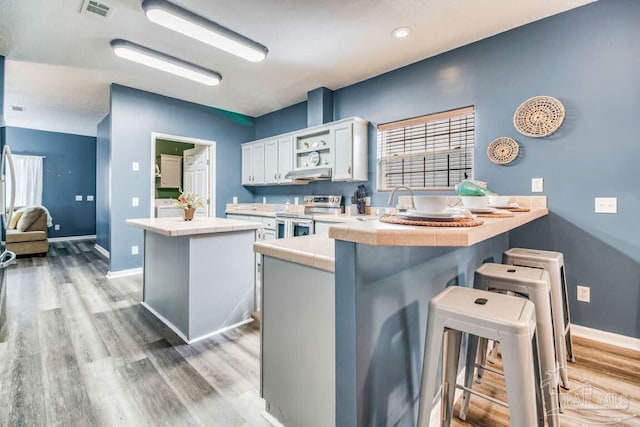 kitchen with white cabinetry, electric range, a kitchen bar, tile countertops, and kitchen peninsula