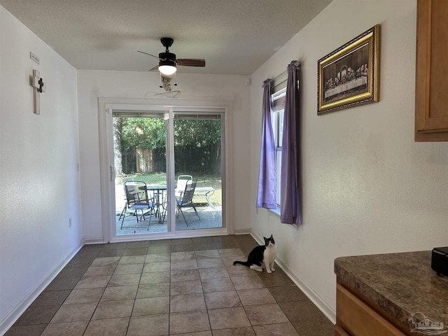 dining room featuring healthy amount of natural light, ceiling fan, baseboards, tile patterned floors, and a textured ceiling