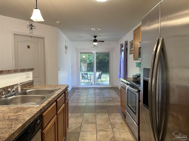 kitchen with appliances with stainless steel finishes, a sink, brown cabinetry, dark countertops, and a ceiling fan