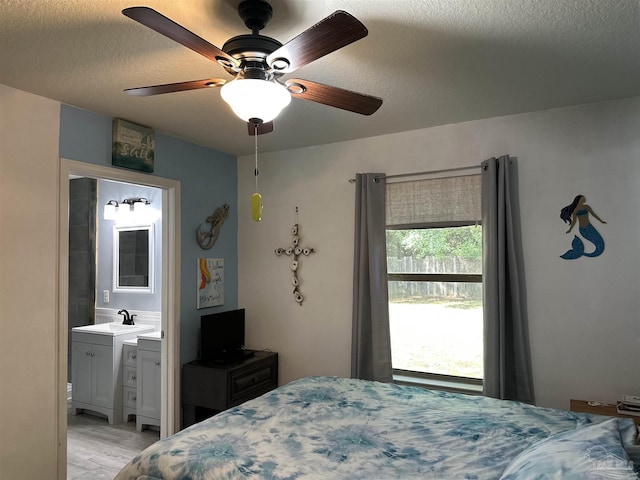 bedroom featuring a sink, connected bathroom, light wood finished floors, a textured ceiling, and a ceiling fan