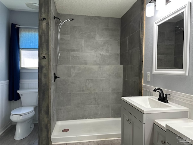 full bathroom with vanity, toilet, tiled shower, wainscoting, and a textured ceiling