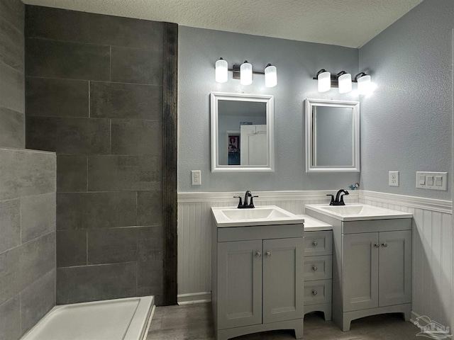 bathroom featuring wainscoting, a tile shower, and two vanities