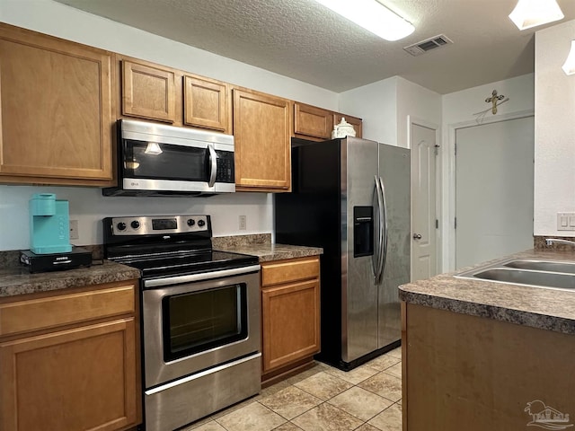 kitchen featuring appliances with stainless steel finishes, a sink, light tile patterned floors, dark countertops, and brown cabinets