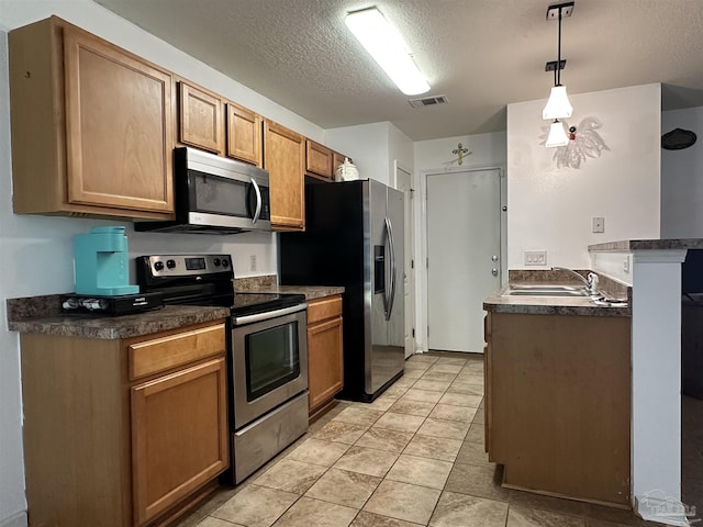 kitchen featuring appliances with stainless steel finishes, dark countertops, a textured ceiling, a sink, and a peninsula