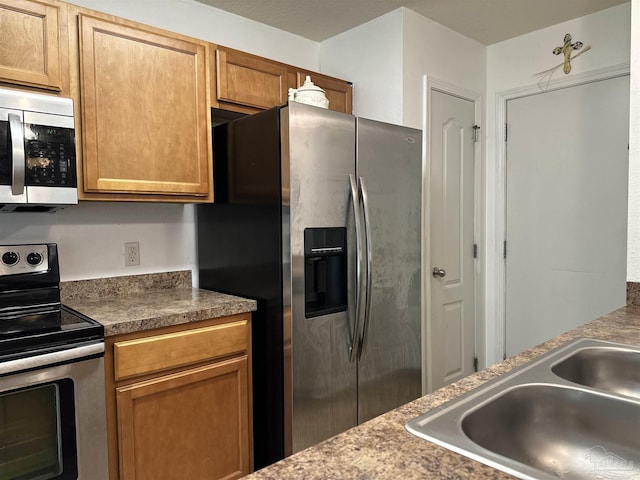 kitchen featuring appliances with stainless steel finishes, a sink, brown cabinets, and dark countertops
